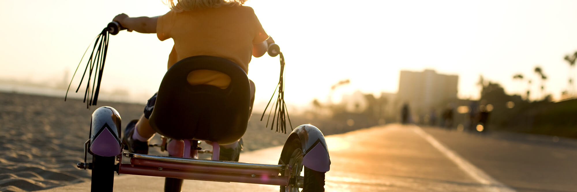 A child riding a tricycle as the sun sets in the background
