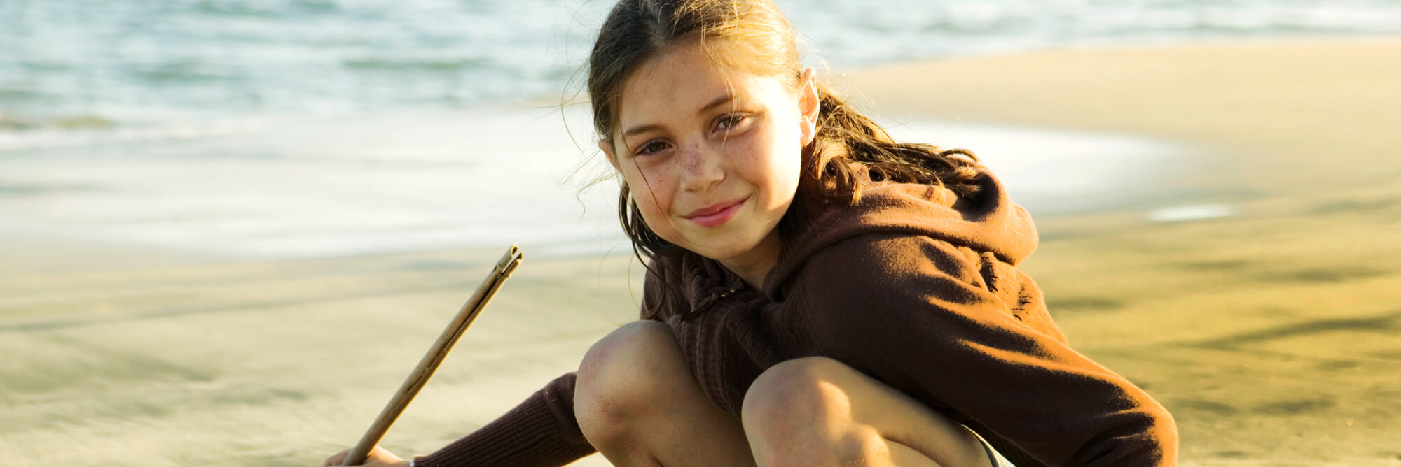 A child drawing in beach sand with a stick