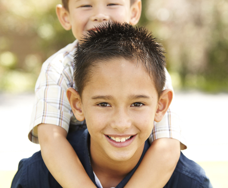 Two boys, one hanging on the others shoulders, smiling