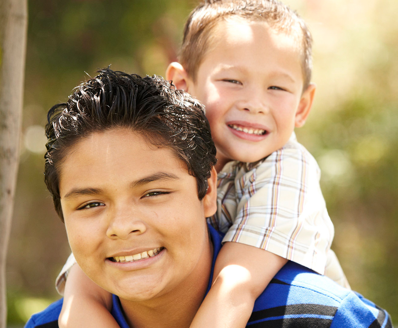 Two boys, the smaller one is drped around the larger one's shoulders