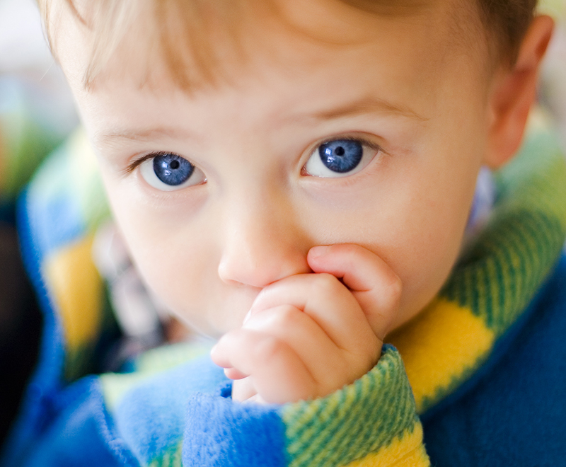 A baby with blue eyes sucking on his fingers