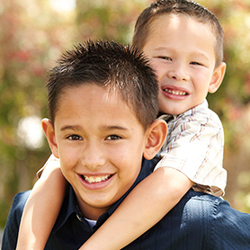 A small child riding on the shoulders of an older boy, both smiling