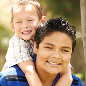 A small child riding on the shoulders of an older boy, both smiling